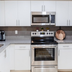 Spacious and well lit kitchen with wood floors and stainless steel appliances. 